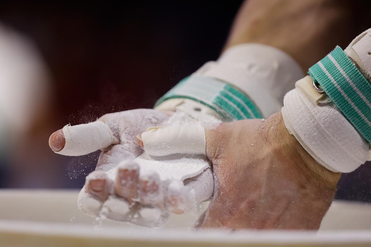 A gymnast applies chalk to his hands